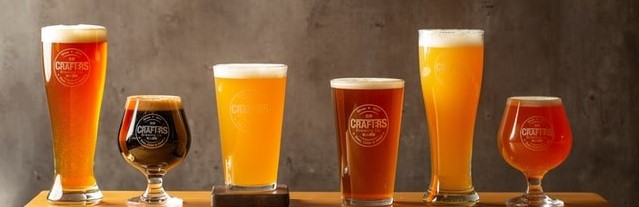 six pints of different craft beers in different glasses, sitting side by side on a wooden bar